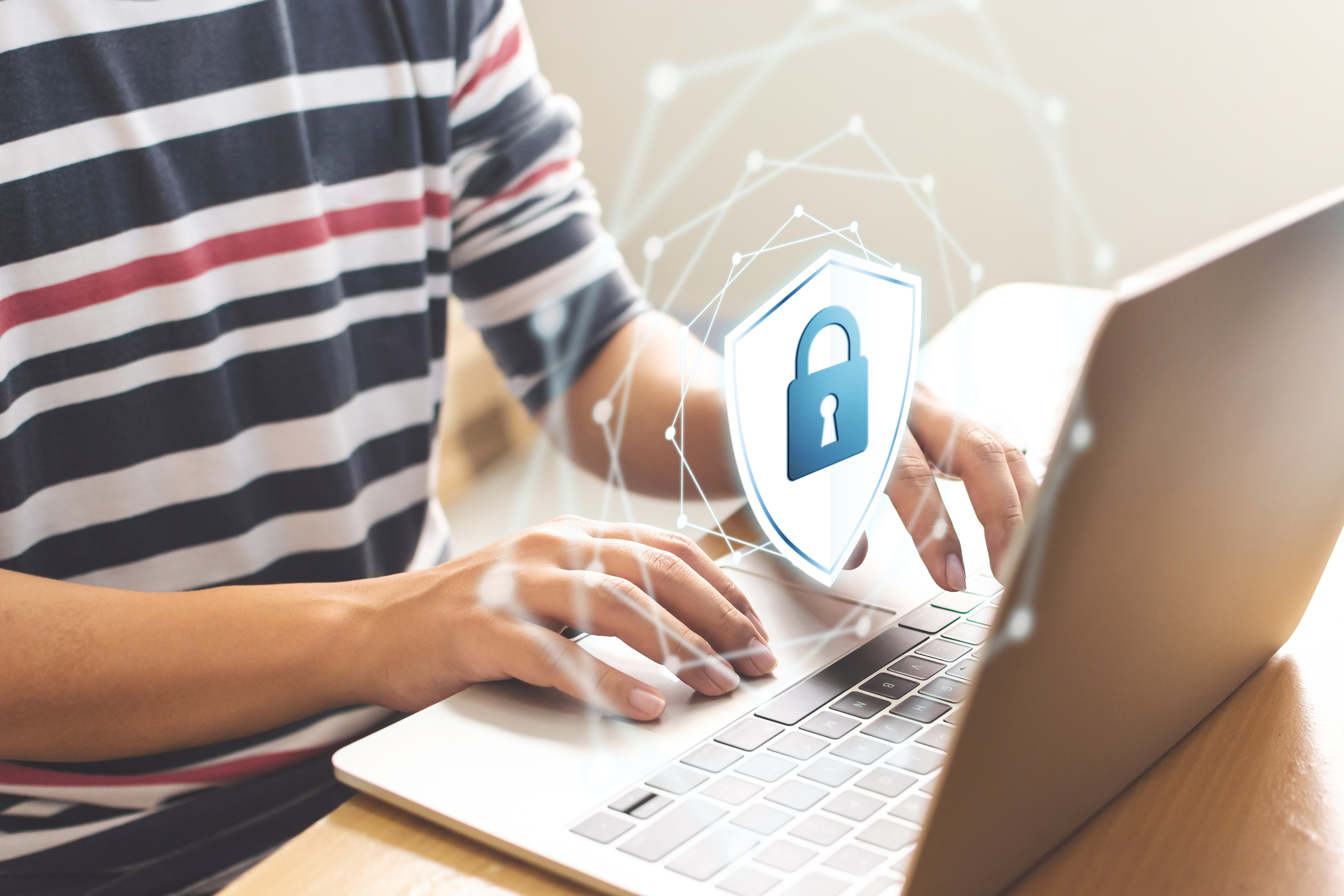 Torso image of a student wearing a striped shirt sitting at a computer with a graphic of a cyber lock symbol floating above the keyboard.