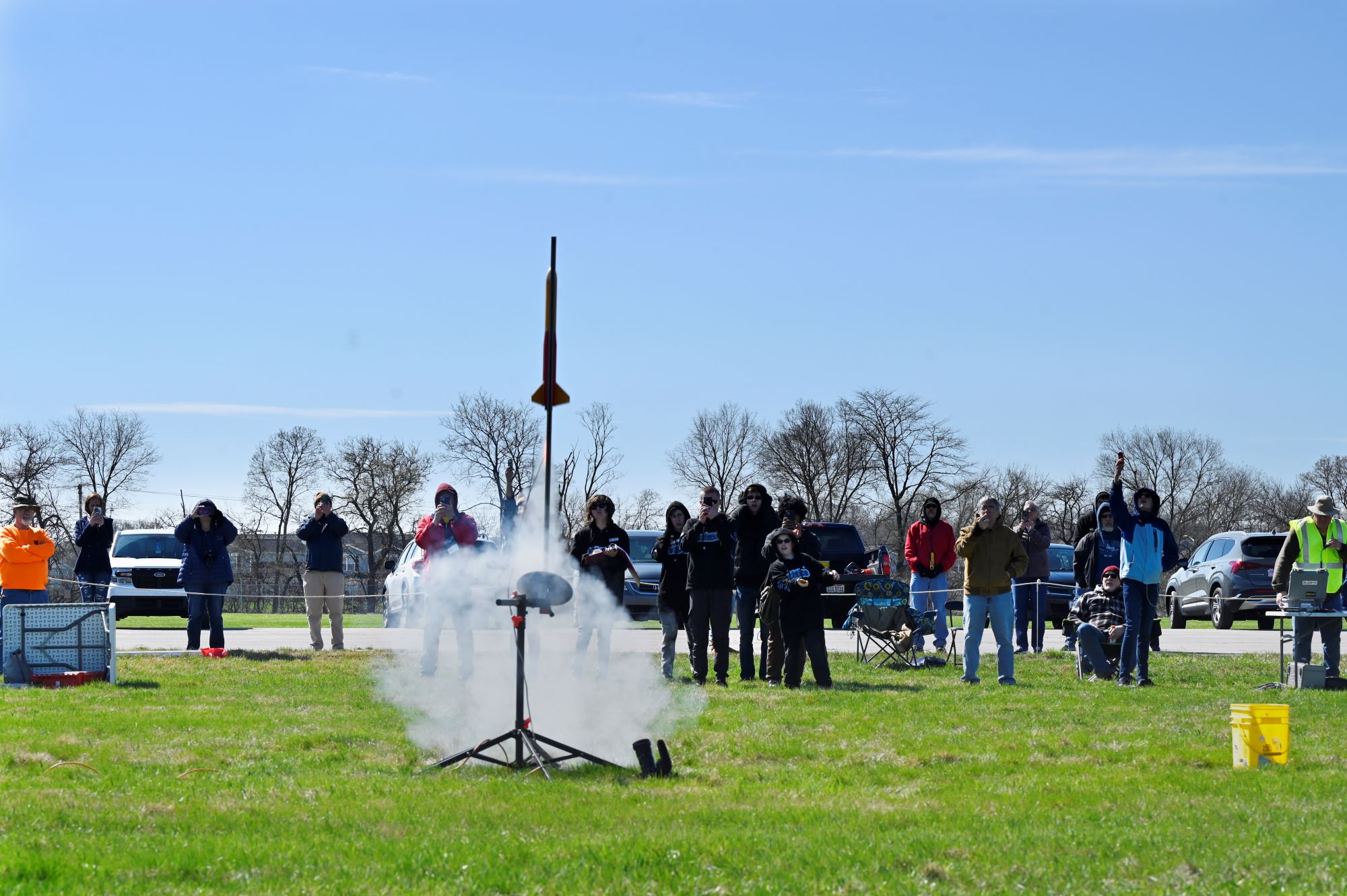 A model rocket is going up to the sky after being launched. A crowd of people stands behind it looking up.