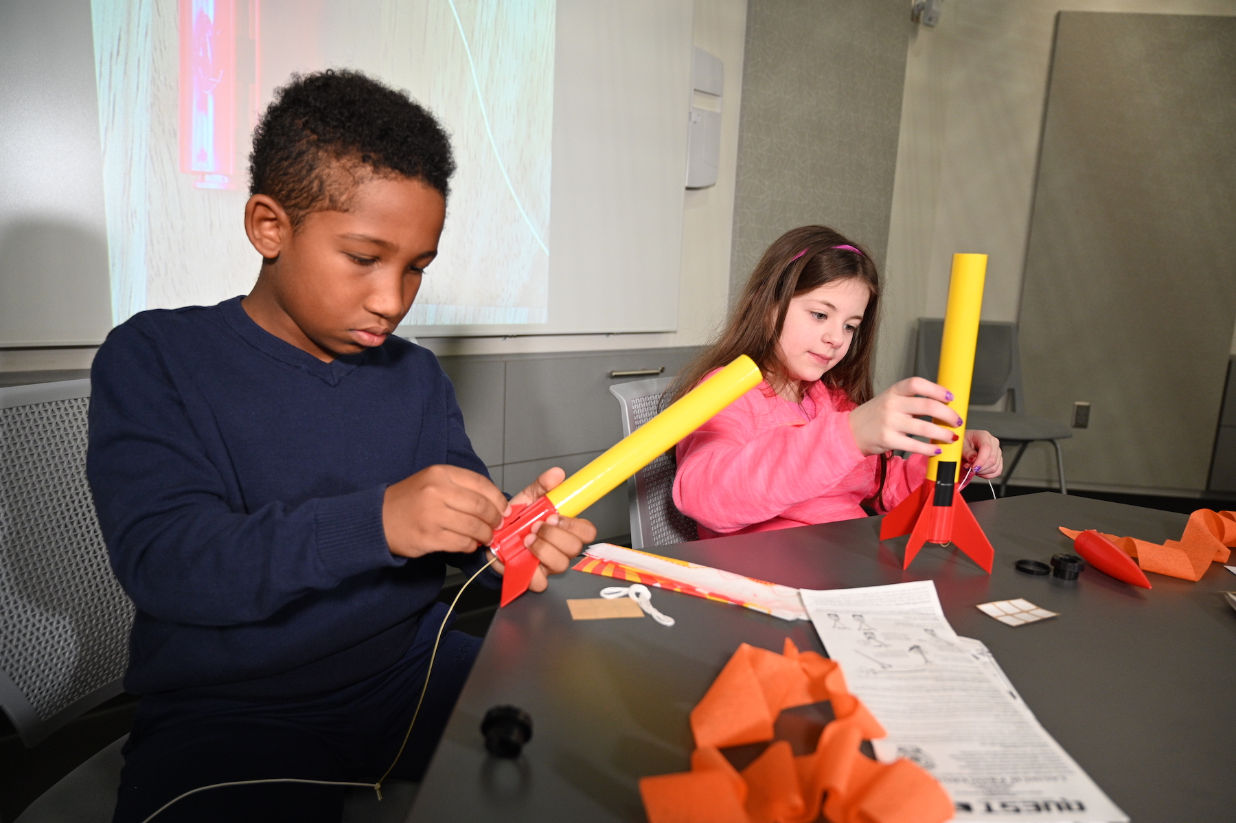 Image of two yound students sitting at a table buidling model rockets.