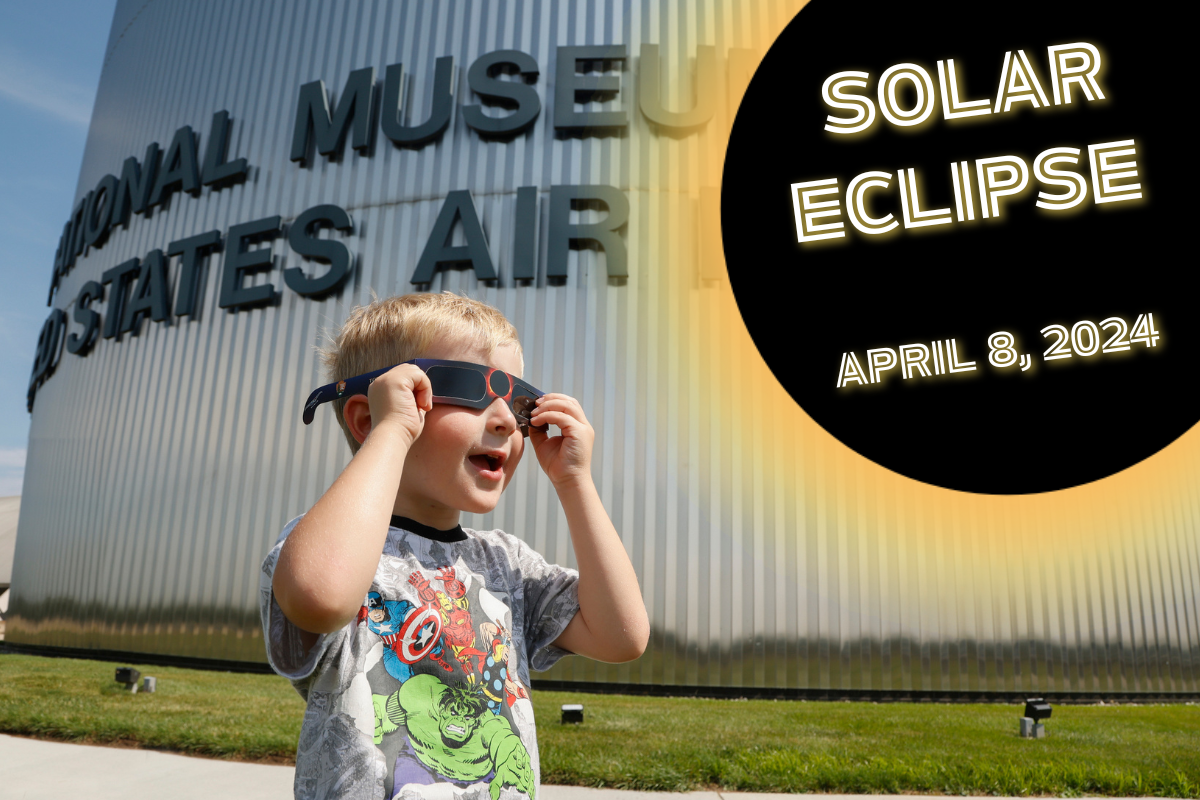 Image of a blond boy wearing eclipse glasses and looking up to the right corner where there is a graphic that says Solar Eclipse, April 8, 2024
