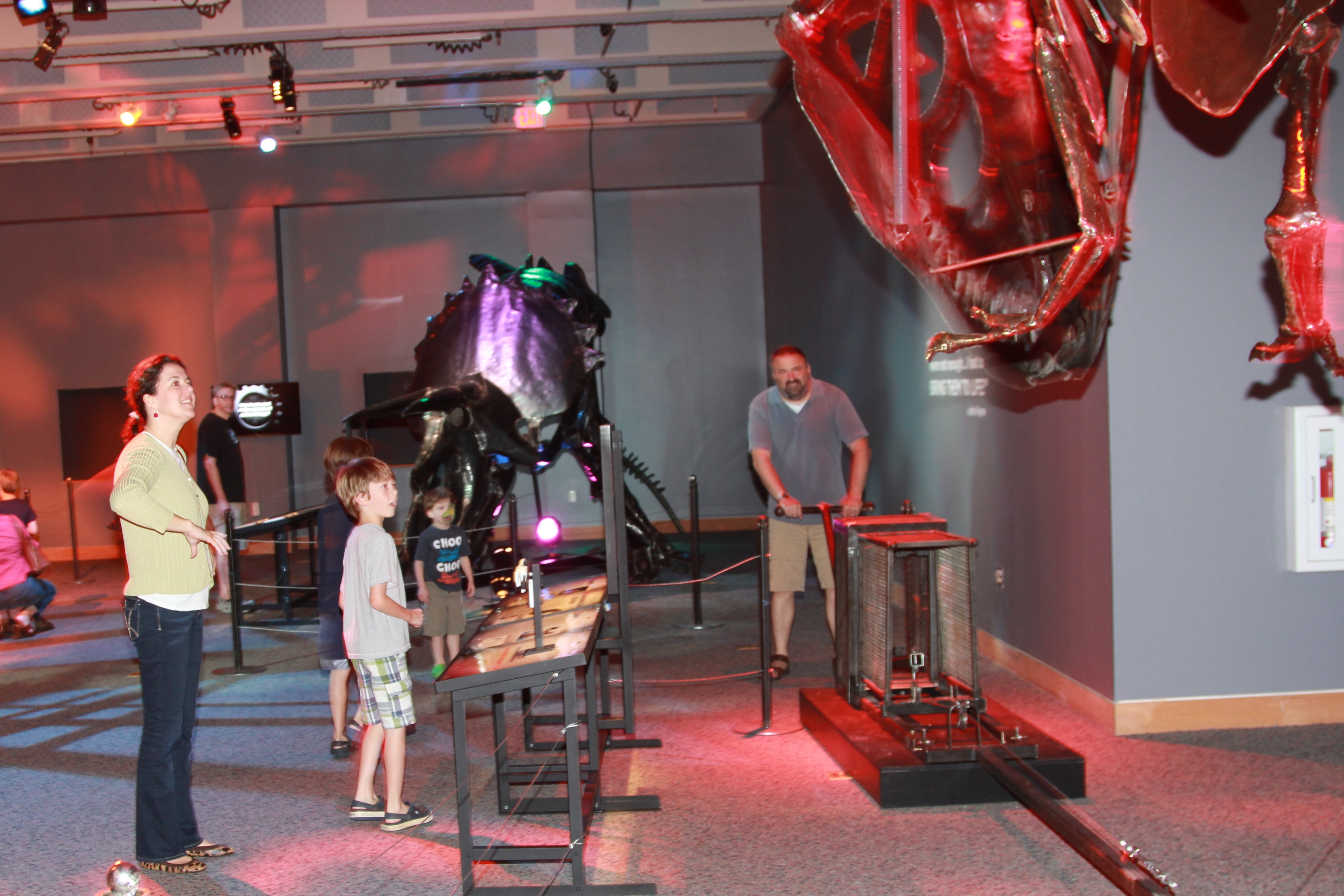 Dinosaurs in Motion. Image of man, woman and young boy standing around the giant TRex scultpure, utilzing the control mechnanism to make it move. 