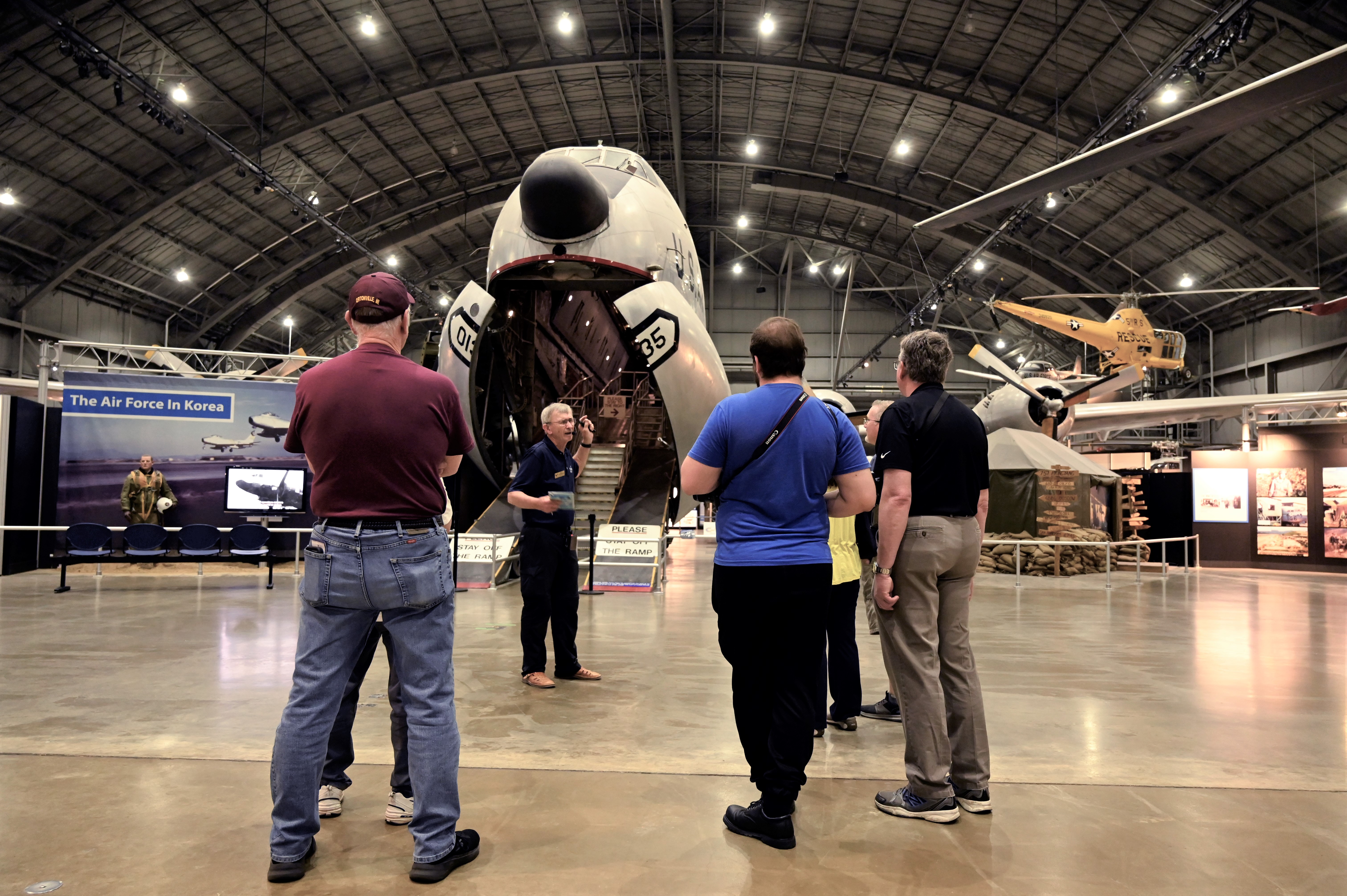 Image of a volunteer in front of the C-24 giving a tour to a group of visitors. In the background is the Korean War Gallery