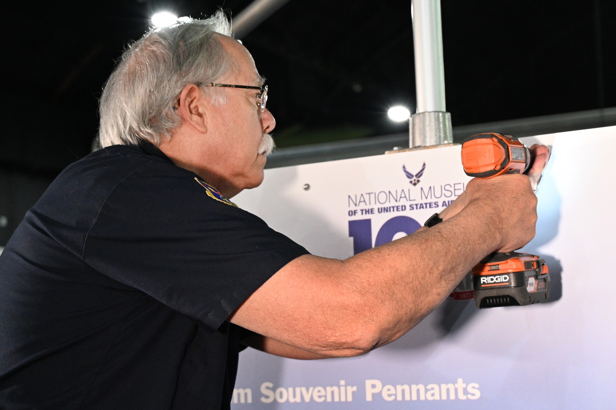 Image of a museum volunteer using a drill to mount a panel on the new centennial exhibit.