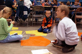 Image of students sitting on the classroom floor with cut out of paper kites